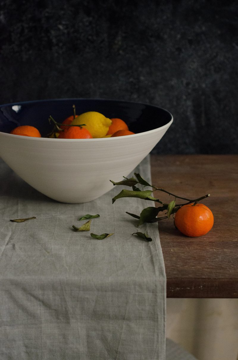 A footed porcelain bowl filled with citrus fruit