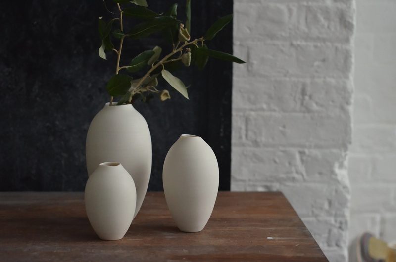 Two porcelain bud vases holding a bare branch against a dark backdrop