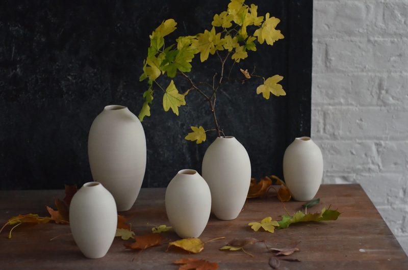 Porcelain bud vases with golden autumn foliage on a dark table